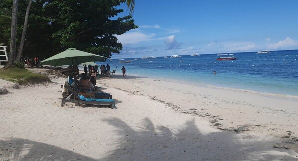 A beach with lounge chairs and umbrellas, a clear view of the ocean, and boats in the distance.