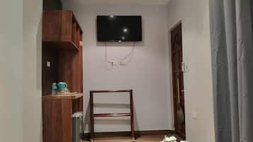 Ett rum med en TV som är monterad på väggen, en trähylla med diverse föremål och en dörr med en kvast lutad mot sig.