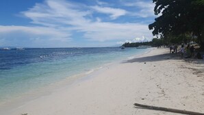 A beach with clear turquoise water, a sandy shore, and boats in the distance. - Alona Beach Poolside Hotel (Panglao)