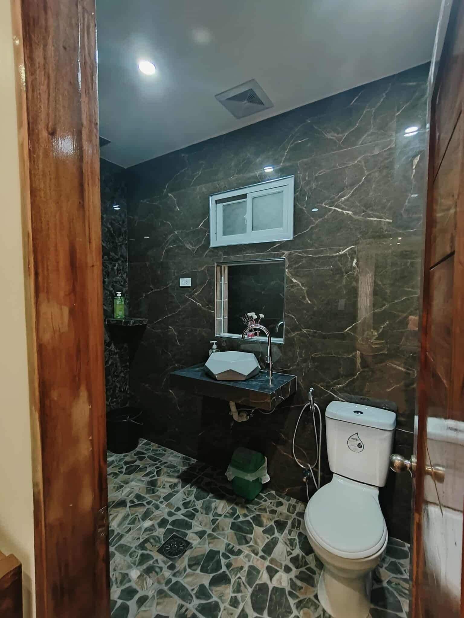 A bathroom with a marble wall, a sink with a mirror, a toilet, and a patterned floor.