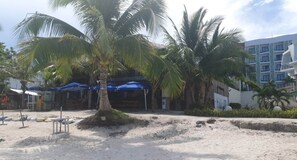 A beachside area with palm trees, a sandy beach, and a building with multiple balconies. - Alona Beach Poolside Hotel (Panglao)