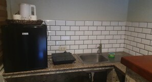 Una cocina con salpicadero de azulejos blancos, un refrigerador negro, un lavabo y una encimera.