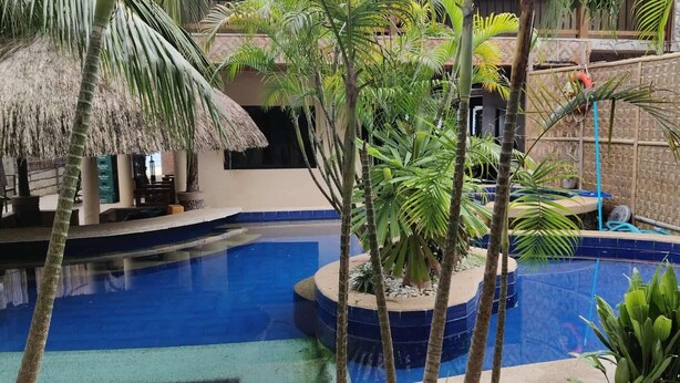 A pool area with a thatched-roof structure, palm trees, and a blue-tiled pool. - Alona Beach Poolside Hotel (Panglao)