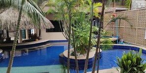 A pool area with a thatched-roof structure, palm trees, and a blue-tiled pool.