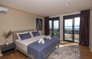 Ein modernes Schlafzimmer mit einem großen Bett, einem Nachttisch, einem Gemälde und Blick ins Freie durch eine Schiebetür.