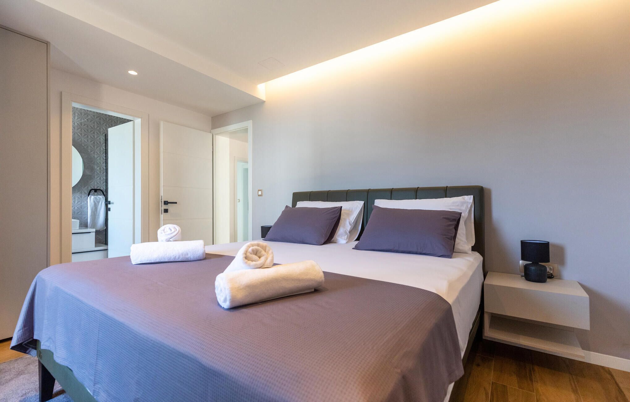 Une chambre d’hôtel moderne avec un grand lit, une table de chevet avec une lampe et vue sur la salle de bain.