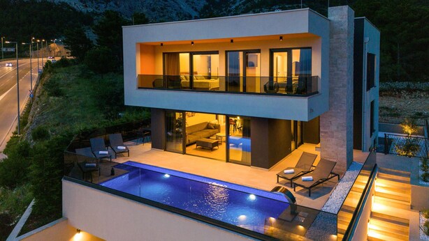 Een modern huis met twee verdiepingen, een glazen balkon, een zwembad en buitenmeubilair.