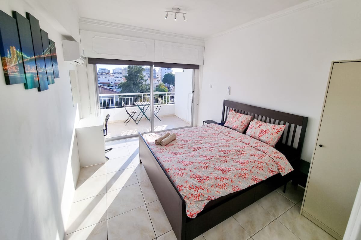 A bedroom with a bed, a balcony, and a cityscape view.