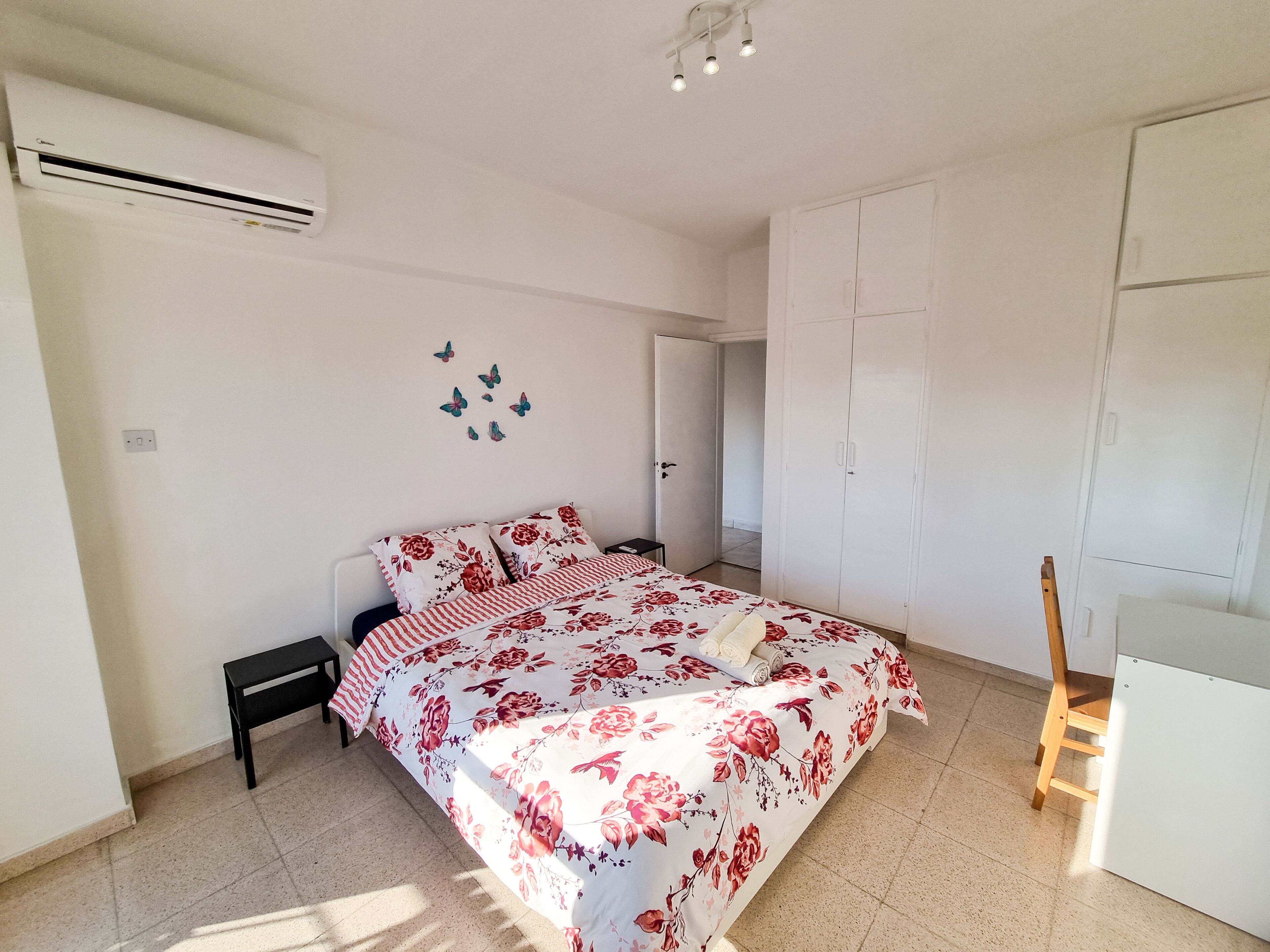 A bedroom with a bed, a nightstand, a wardrobe, and an air conditioning unit.