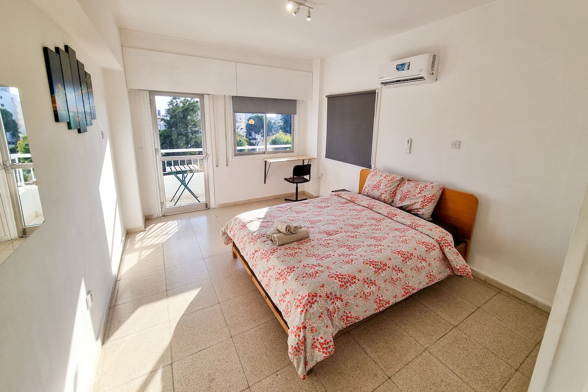 A bedroom with a bed, a desk, and a balcony.