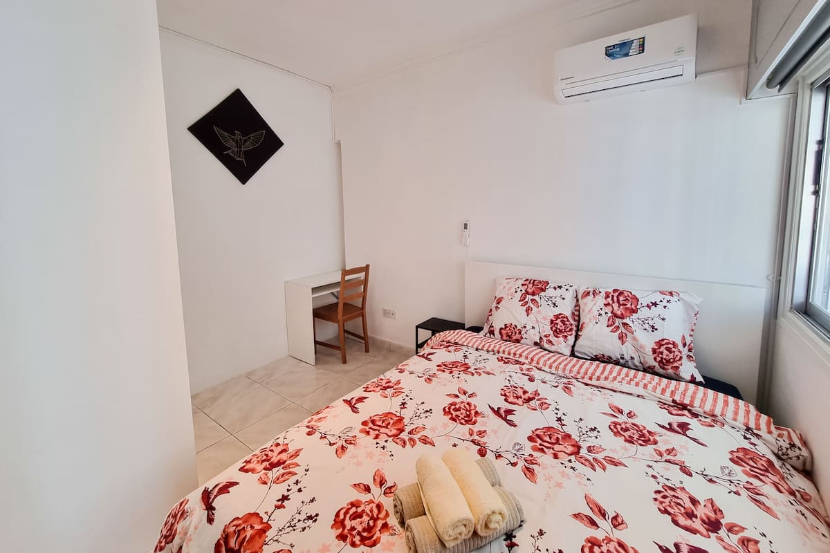 A bedroom with a bed, a desk, and an air conditioning unit.