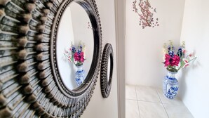 A mirror with a decorative frame, a wall with a floral decal, and two vases with flowers. - City View Rooms (Larnaca)