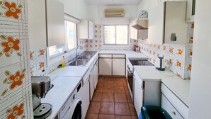 A compact kitchen with white cabinets, a built-in washing machine, and a window providing natural light. - City View Rooms (Larnaca)