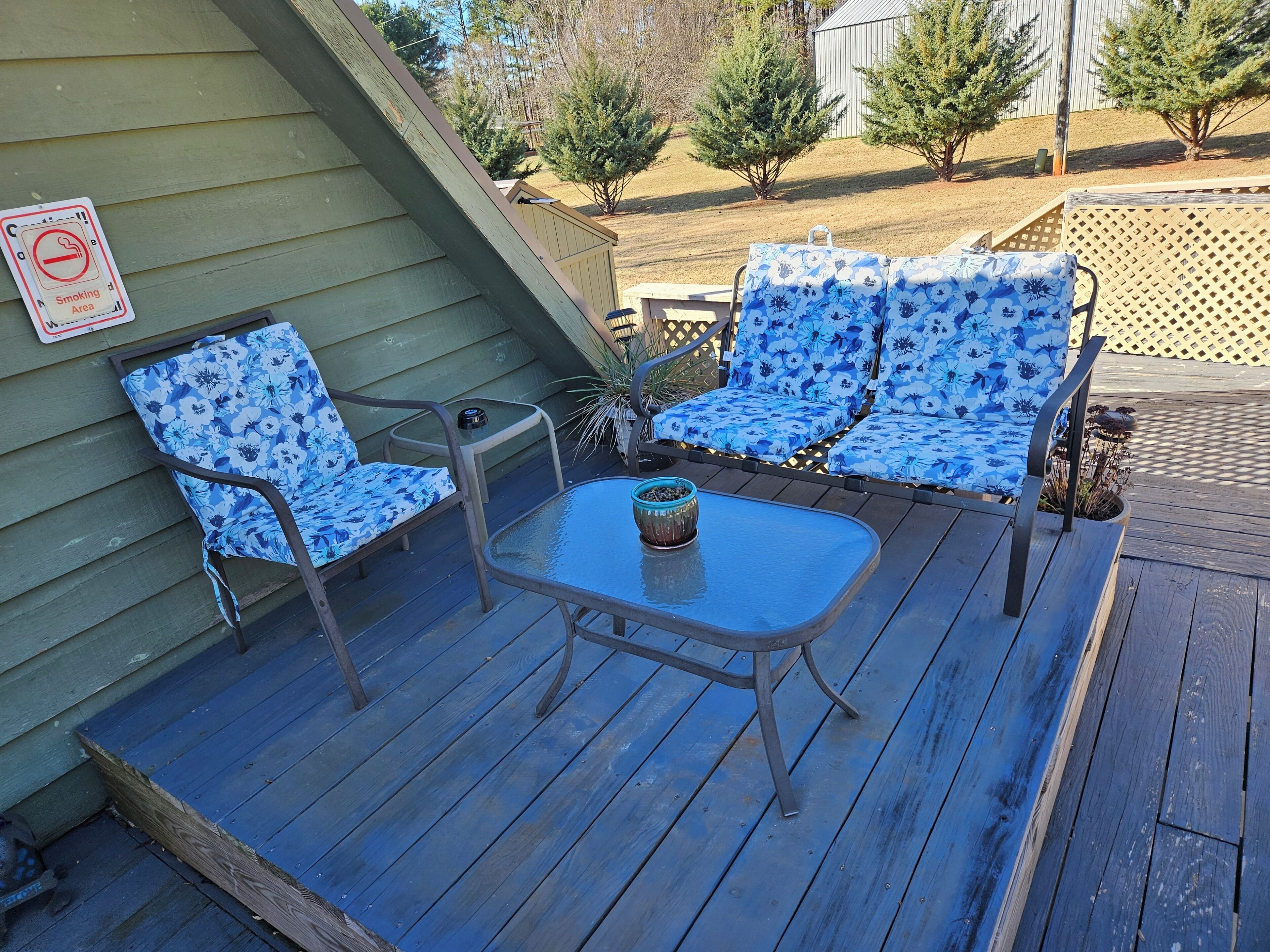 Une terrasse avec deux chaises bleues à motifs floraux et une petite table, un panneau «interdiction de fumer» sur le mur, et une terrasse en bois.