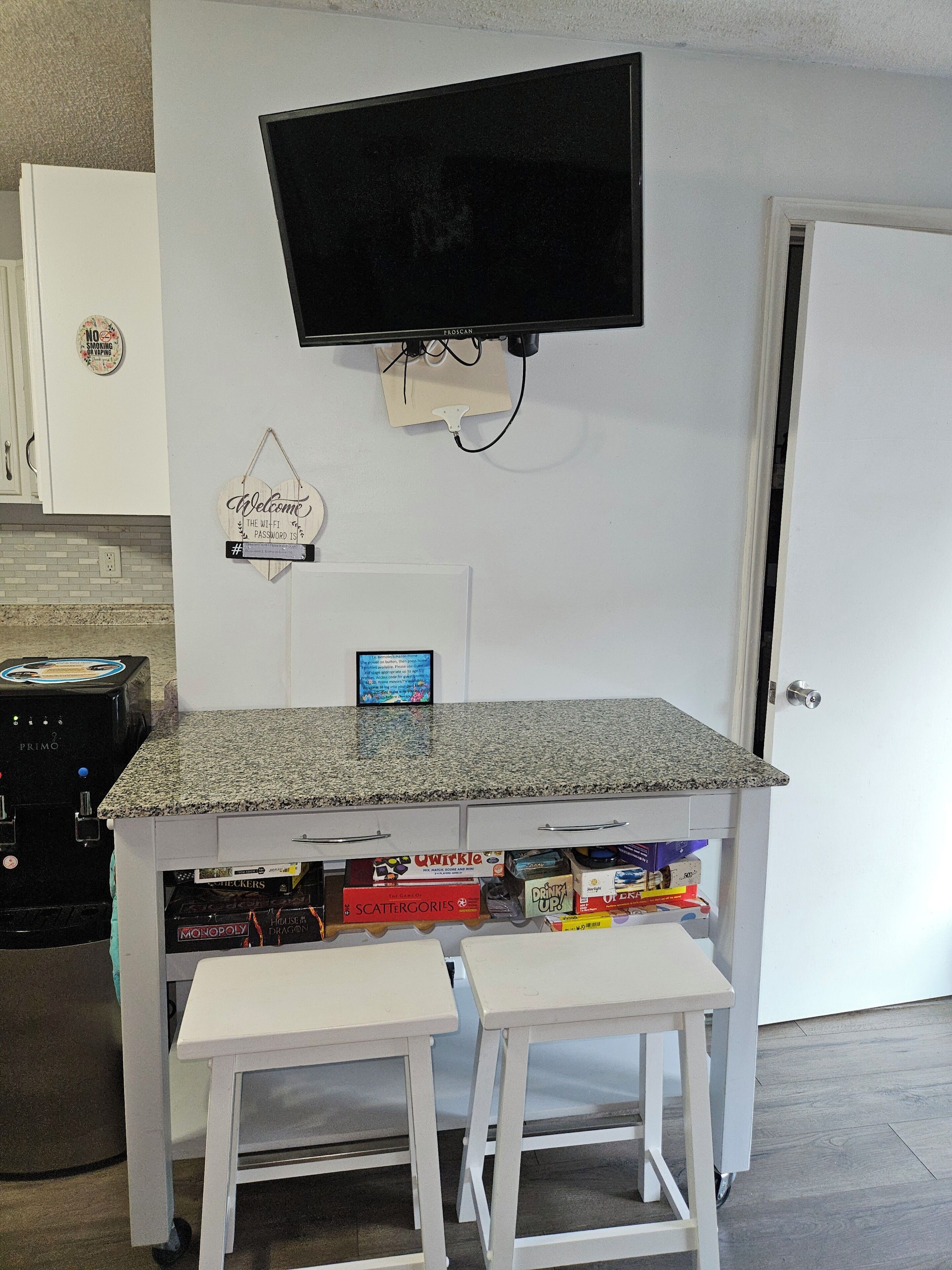A kitchen area with a TV mounted on the wall, a coffee machine, and a small table with stools.