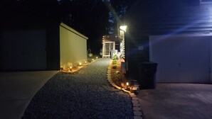 Un camino de entrada que lleva a un garaje, con un sendero de grava y pequeñas luces a los lados.