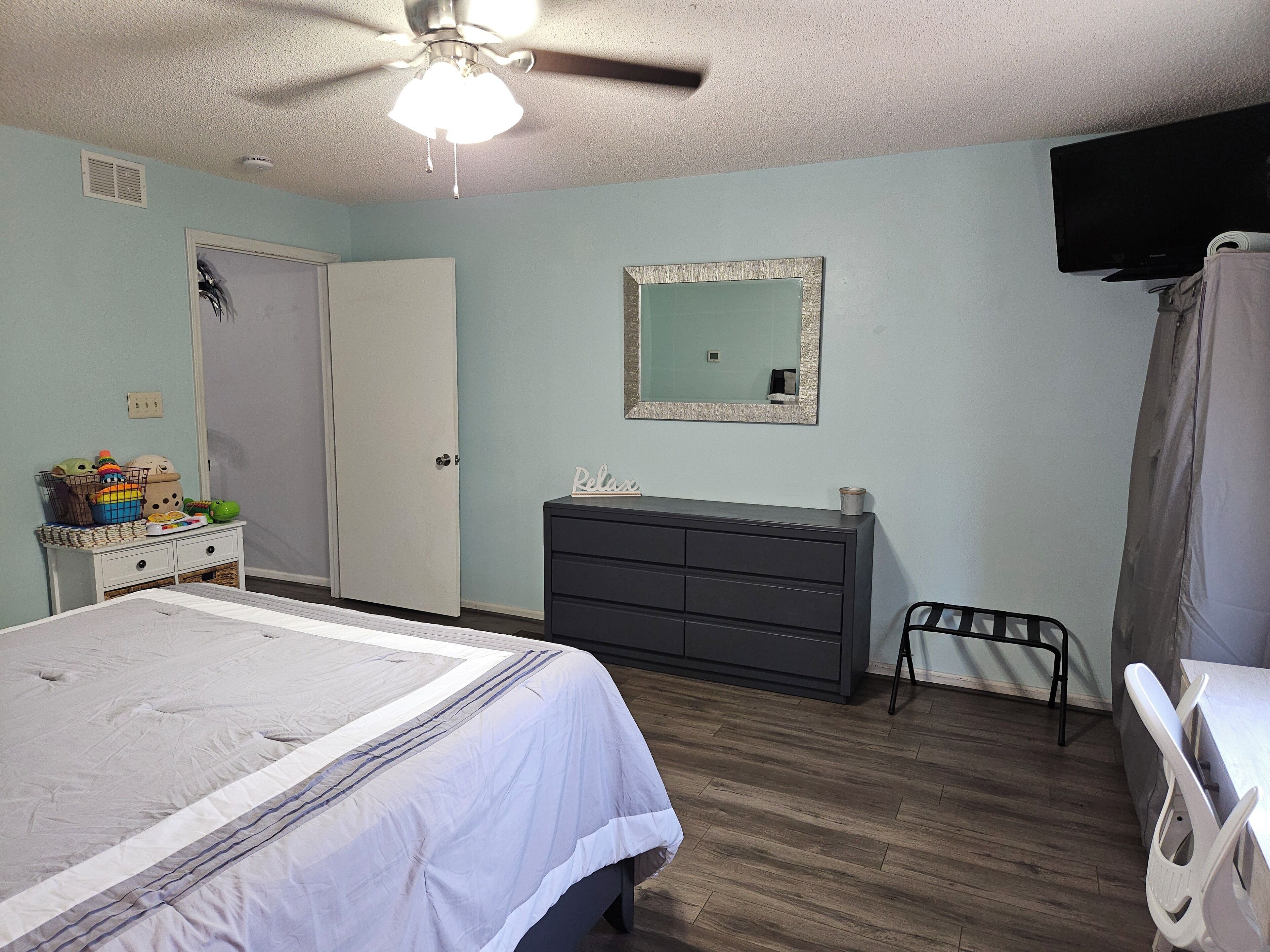 Une chambre à coucher comprenant un lit, une commode, un miroir, un ventilateur de plafond et un téléviseur.