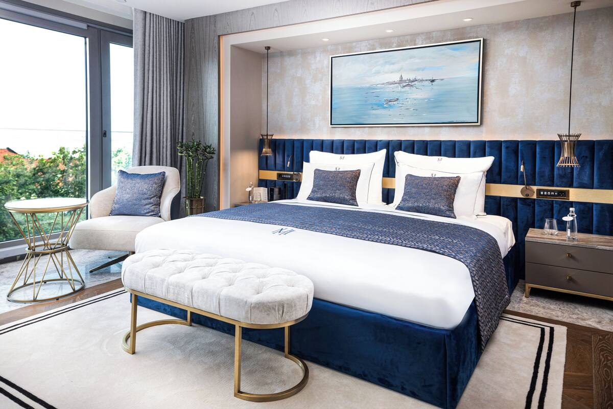 A modern bedroom with a large bed, a sofa, a side table, and a view of the outdoors.