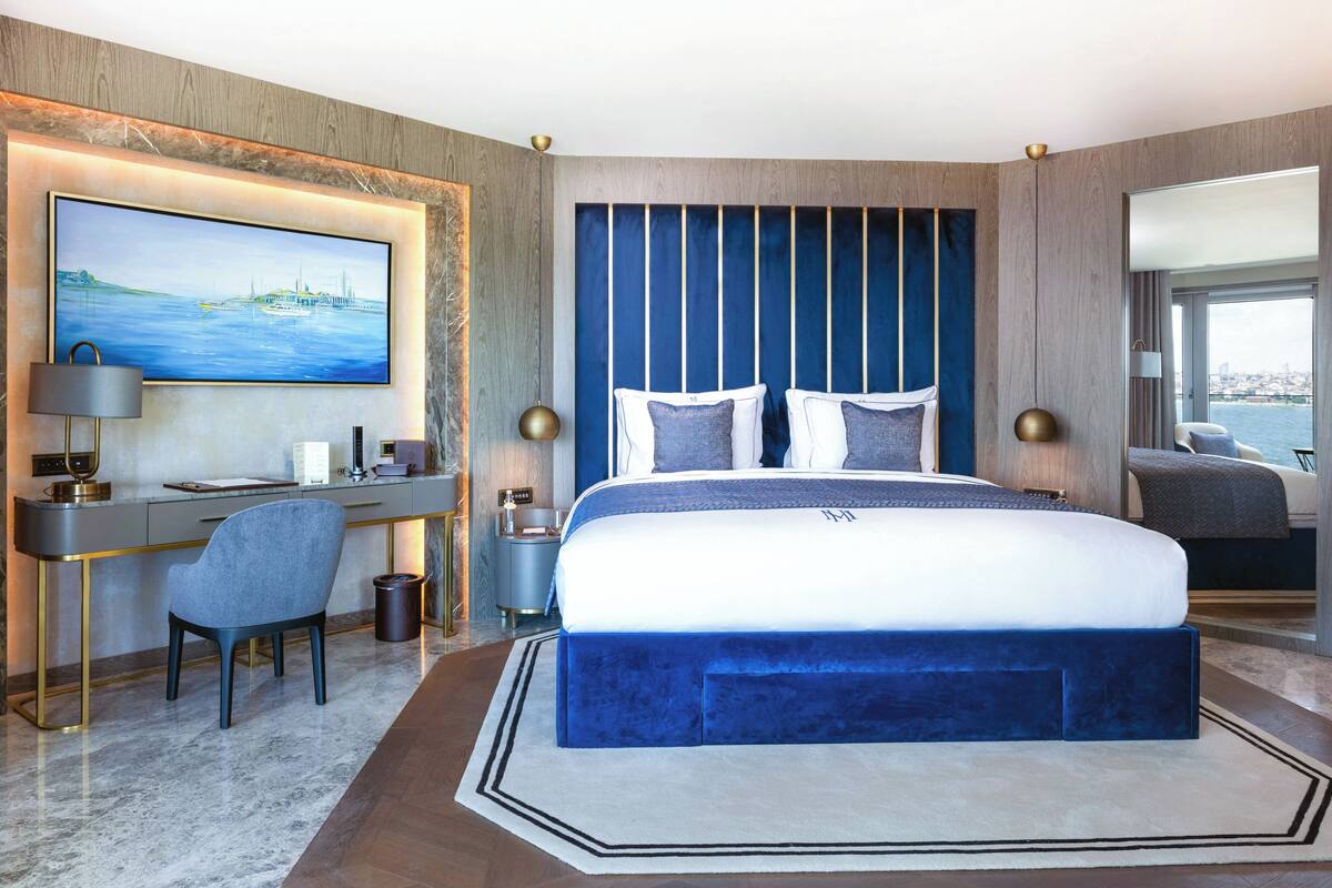 A modern hotel room with a large bed, a desk, and a view of the city.