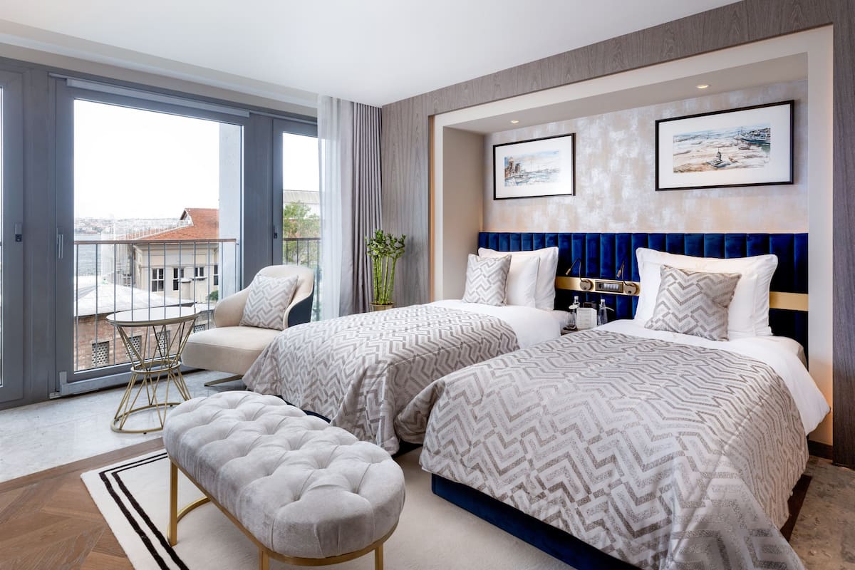 A modern hotel room with two beds, a balcony, and a view of the city.
