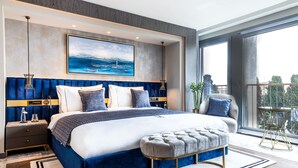 A modern bedroom with a large bed, a headboard with vertical lines, a bedside table, a bench, and a view of the outdoors through a large window. - The Maestro Hotel (Istanbul)