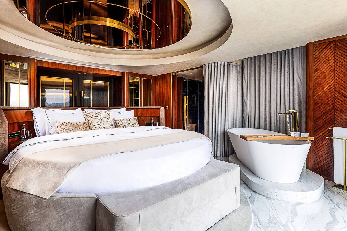 A luxurious bedroom with a large bed, a modern bathtub, and a view of the outdoors.