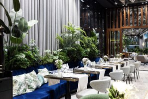 A modern restaurant with blue upholstered seating, white tablecloths, and lush green plants. - The Maestro Hotel (Istanbul)