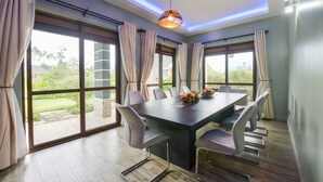 A spacious dining area with a large table and chairs, large windows with curtains, and a decorative hanging light fixture. - Kabale Safari Club (Kabale)