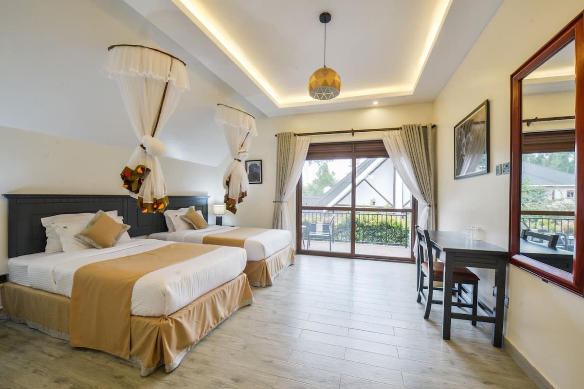 A hotel room with two beds, a balcony, a desk, and a large window.