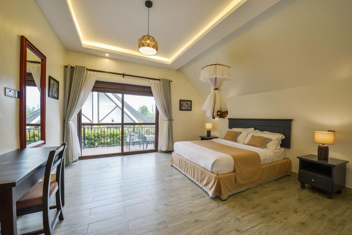 A hotel room with a large bed, a desk, and a balcony with curtains.