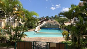 A swimming pool with a slide, surrounded by palm trees and a gated entrance. - Appartements - Le Paradisier Ambatobe (Antananarivo)
