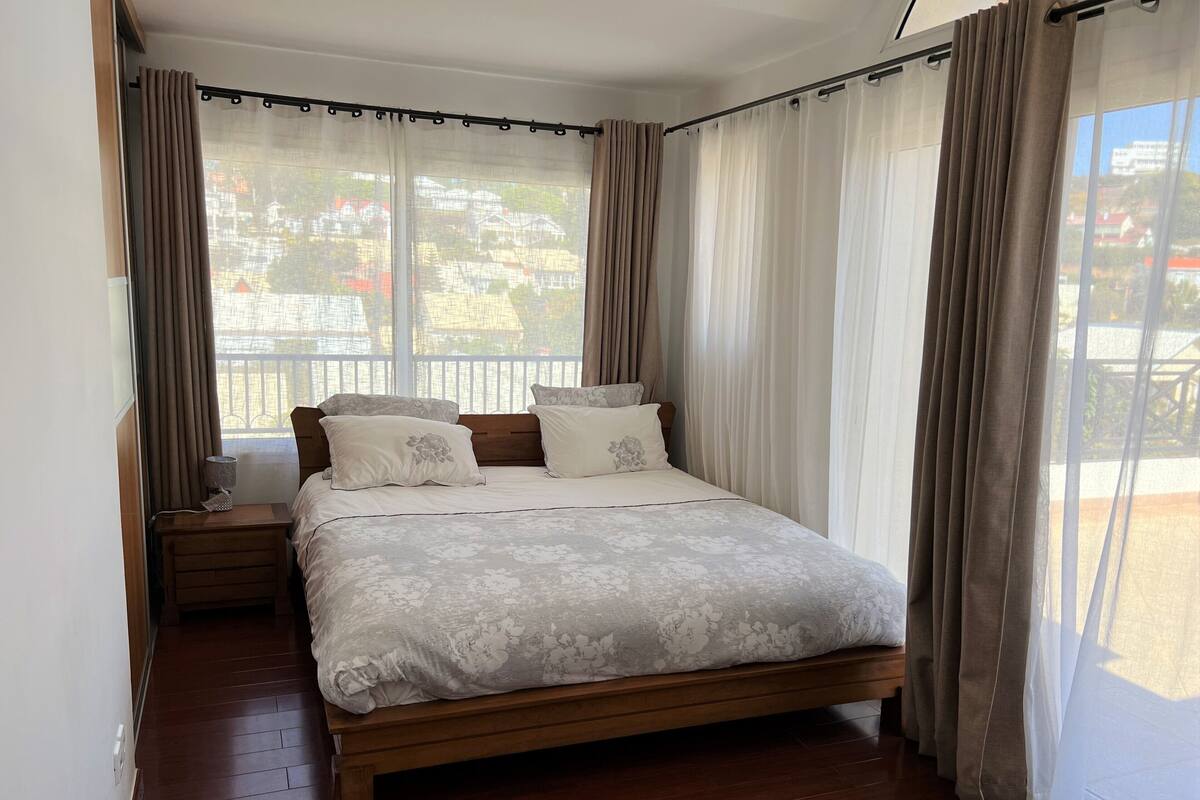 A bedroom with a wooden bed, white bedding, and a view of a balcony.