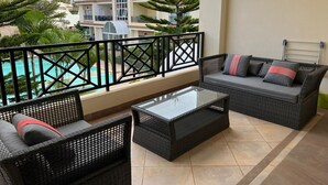 A balcony with wicker furniture, a glass table, and a view of a pool and buildings. - Appartements - Le Paradisier Ambatobe (Antananarivo)