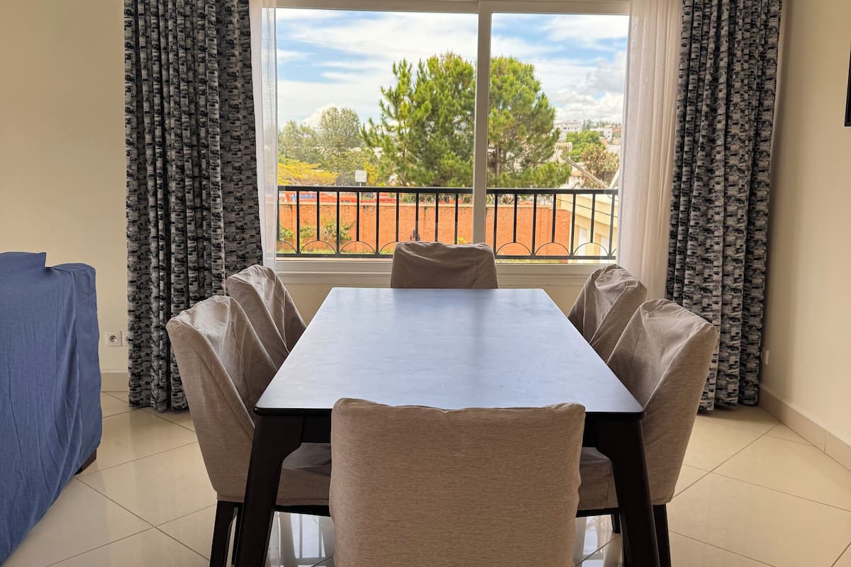 A dining area with a table and chairs, a view of the outside, and a balcony with a railing.