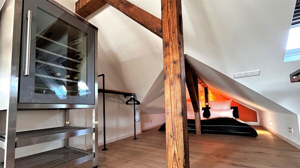 A modern loft bedroom with a skylight, wooden beams, and a mezzanine with a metal railing. - HLH - Exclusiv Selection (Freiburg im Breisgau)