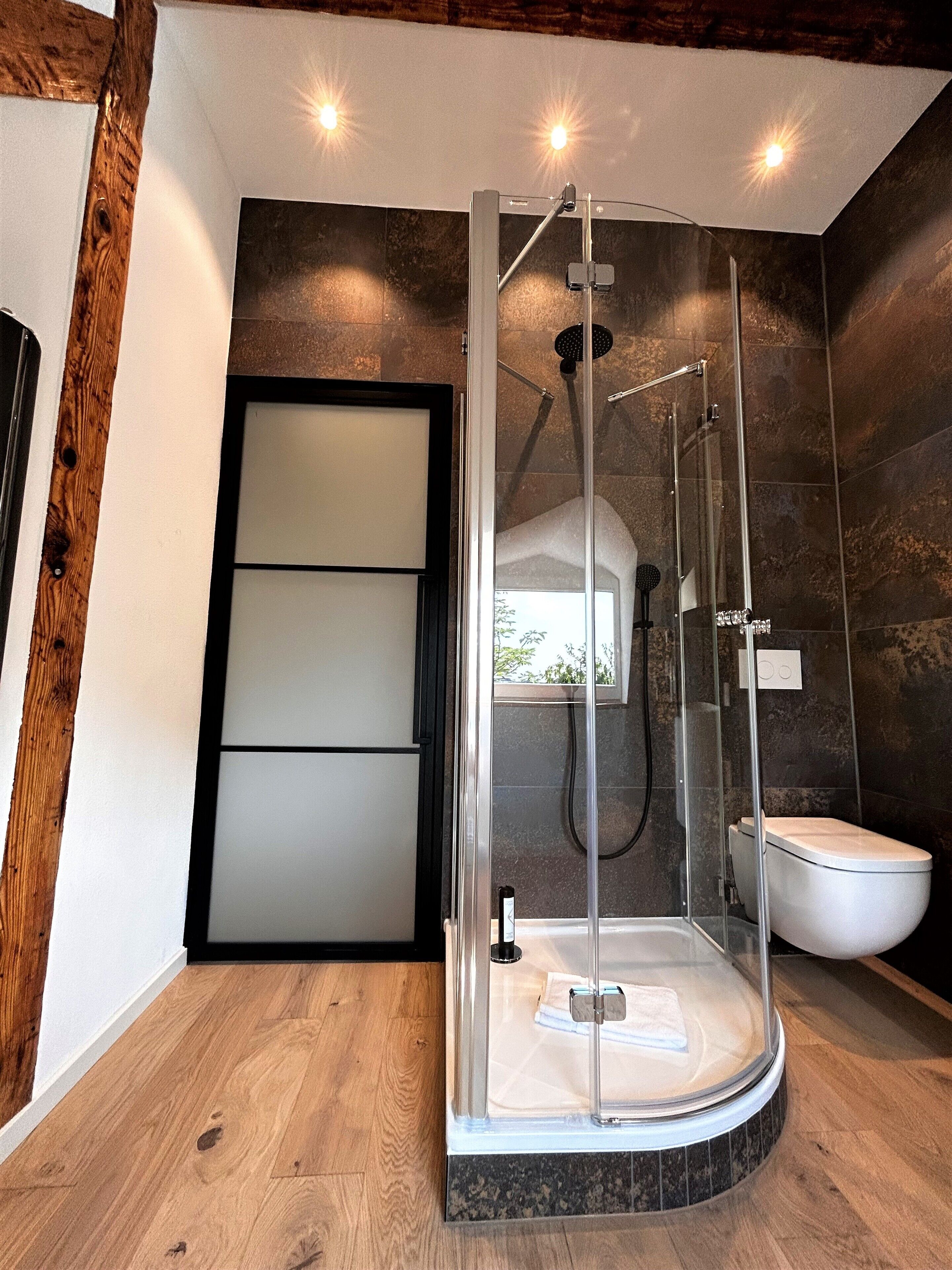 A modern bathroom with a glass-enclosed shower, a white sink, and a wooden floor.