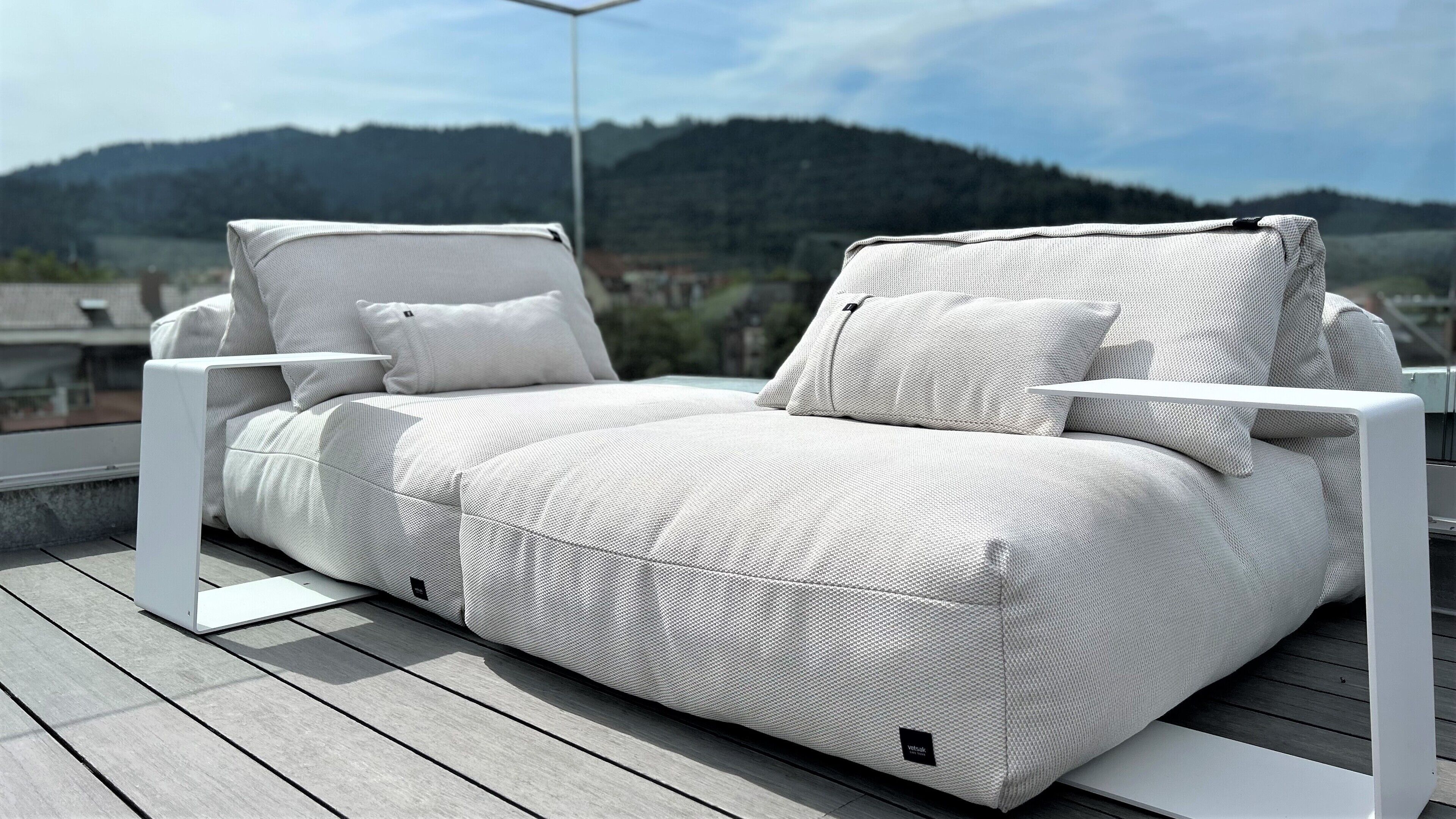 A white outdoor sofa with cushions on a wooden deck, overlooking a mountainous landscape.