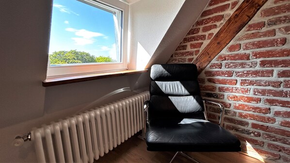 A corner room with a sloped ceiling, a radiator, a window with a view of greenery, and a brick wall. - HLH - Exclusiv Selection  (Freiburg im Breisgau)