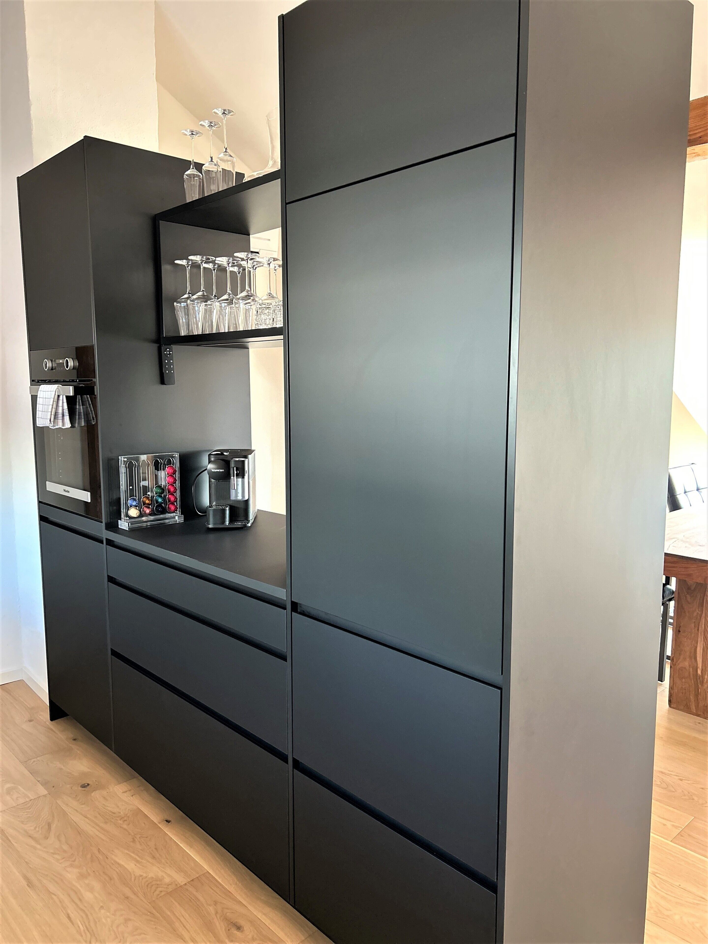 A modern kitchen with a black refrigerator, a coffee machine, and a shelf with wine glasses.