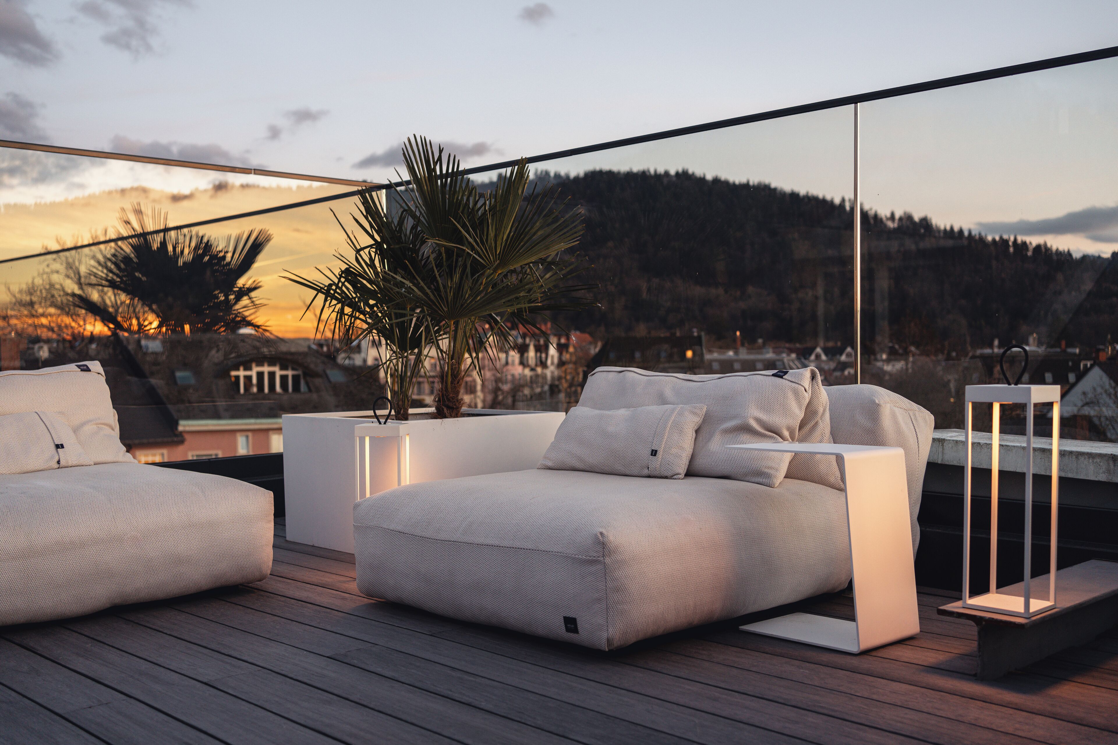 Un espacio exterior moderno con sala y mesita auxiliar, con vistas a un paisaje pintoresco de árboles y colinas.