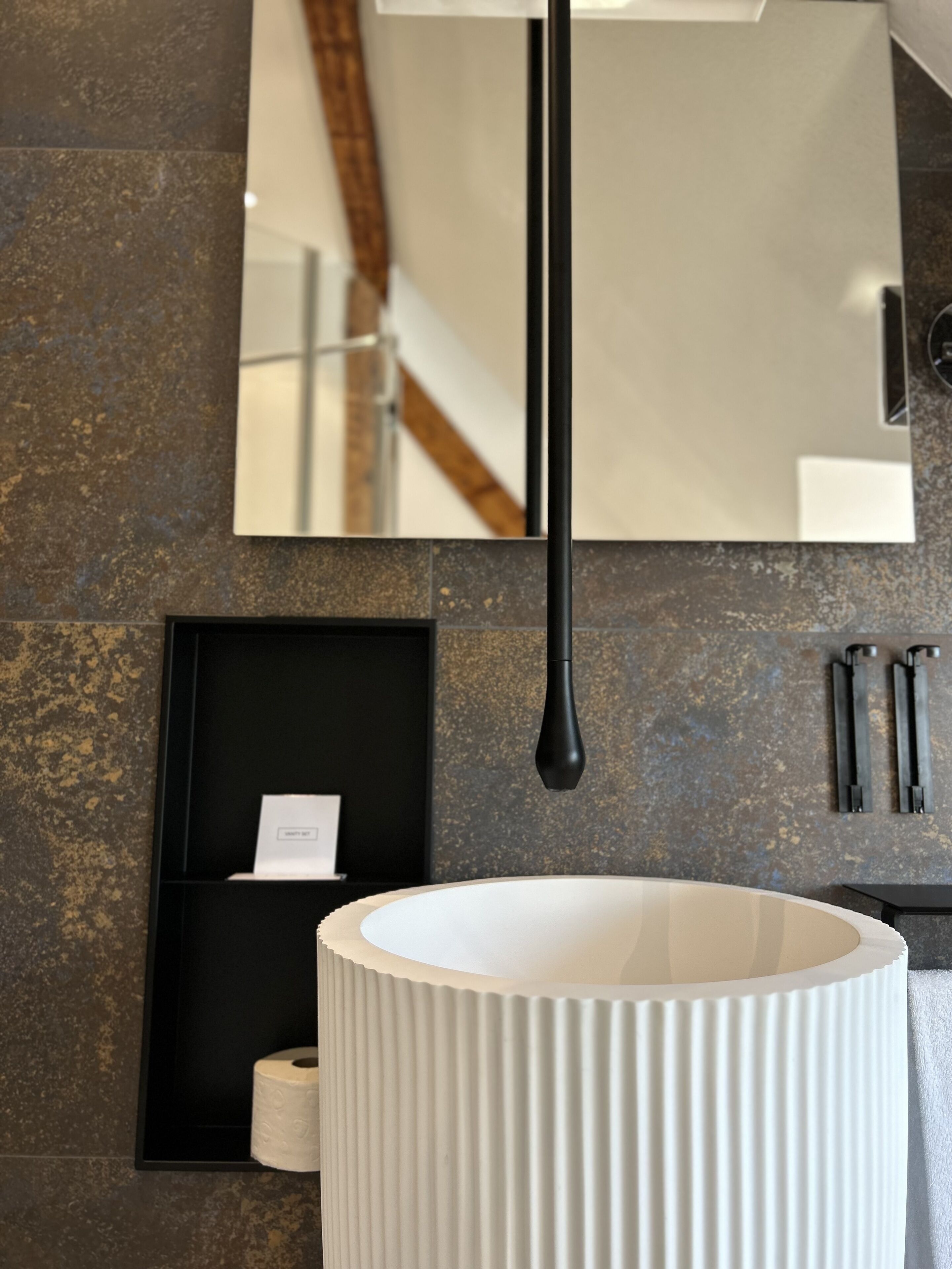 Un baño con un espejo grande, un lavabo blanco y un perchero negro.