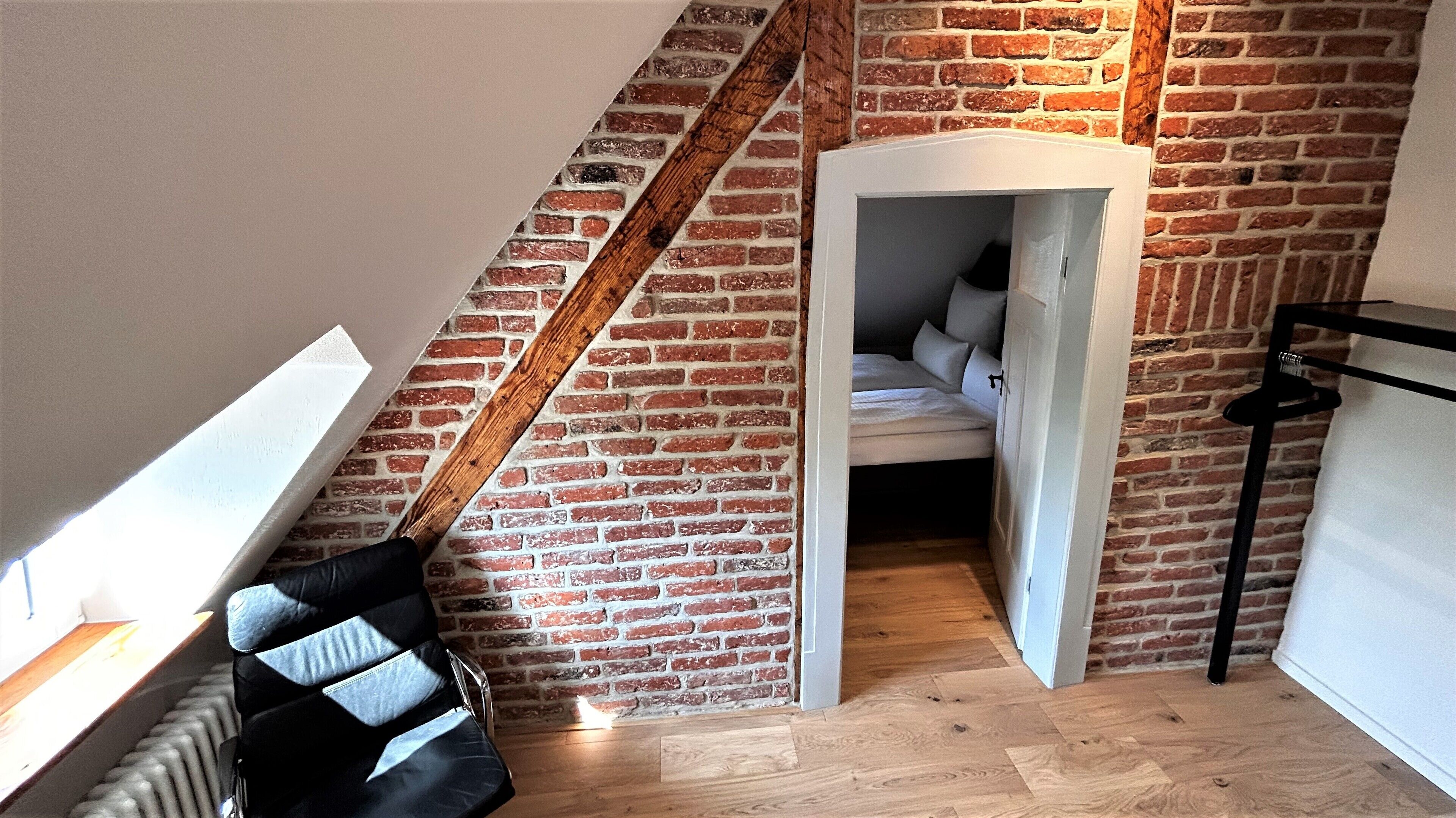 A loft bedroom with exposed brick walls, a sloped ceiling, and a small sleeping area with a bed and pillows.