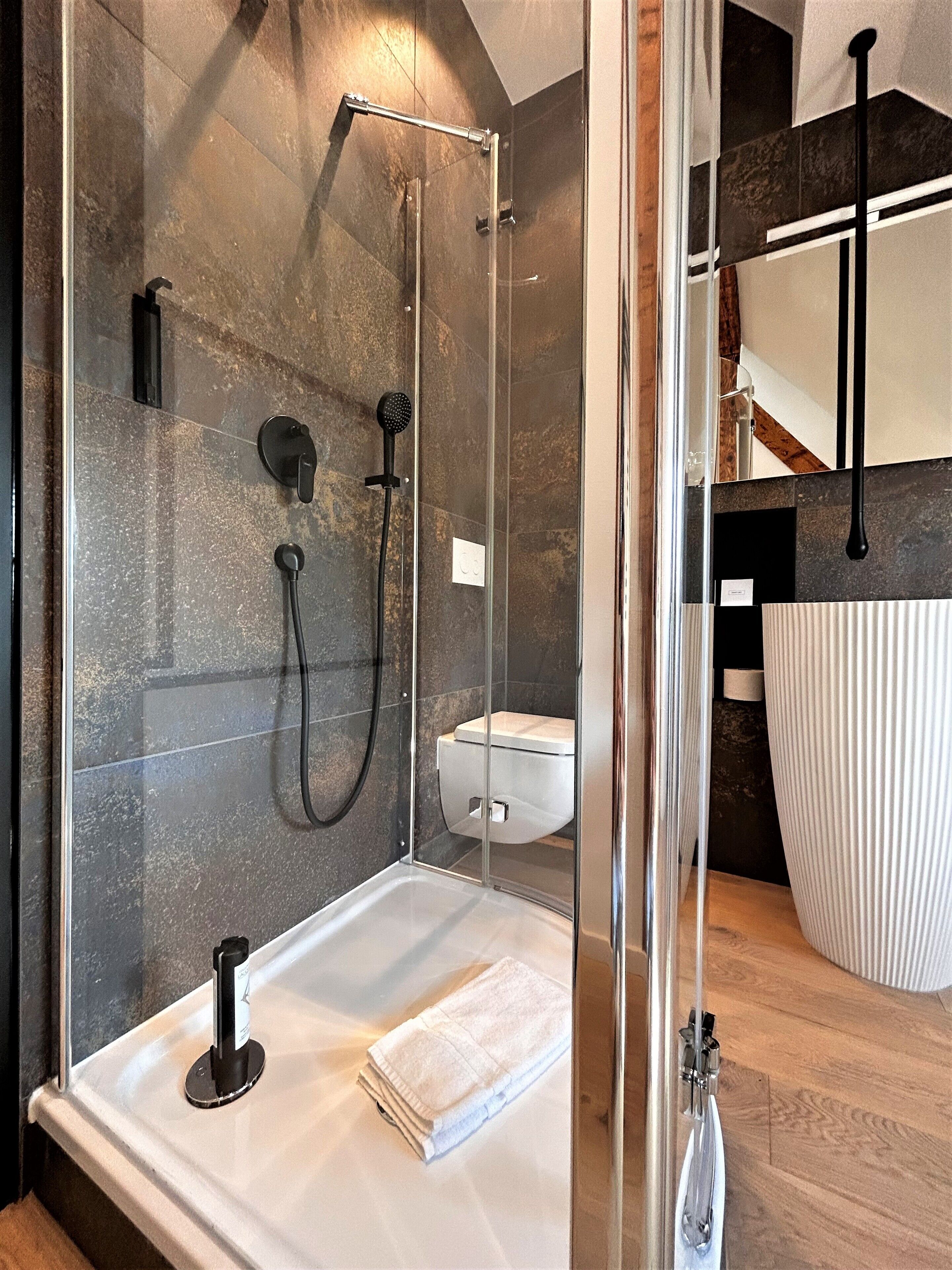 Ein modernes Badezimmer mit einer gläsernen Duschkabine, einer weißen Toilette und einer großen weißen Vase.