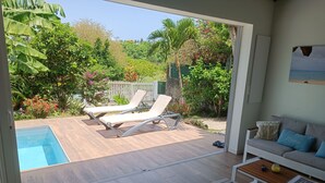 Un espace de vie extérieur moderne comprenant une piscine, des chaises longues et un coin salon avec une table et des coussins.