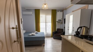 Una habitación de hotel con cama, una silla, kitchenette y ventana con cortinas.