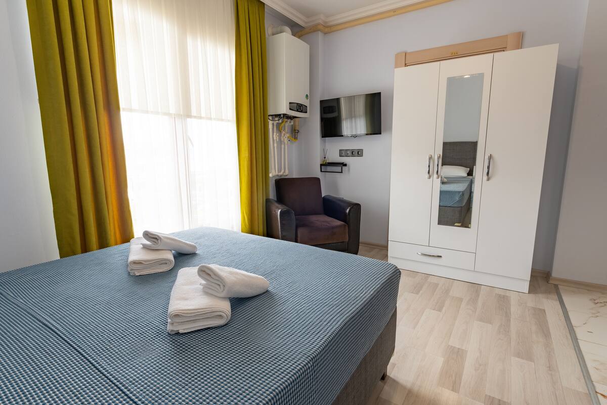 Una habitación de hotel con una cama, una silla, un armario y un televisor montado en la pared.