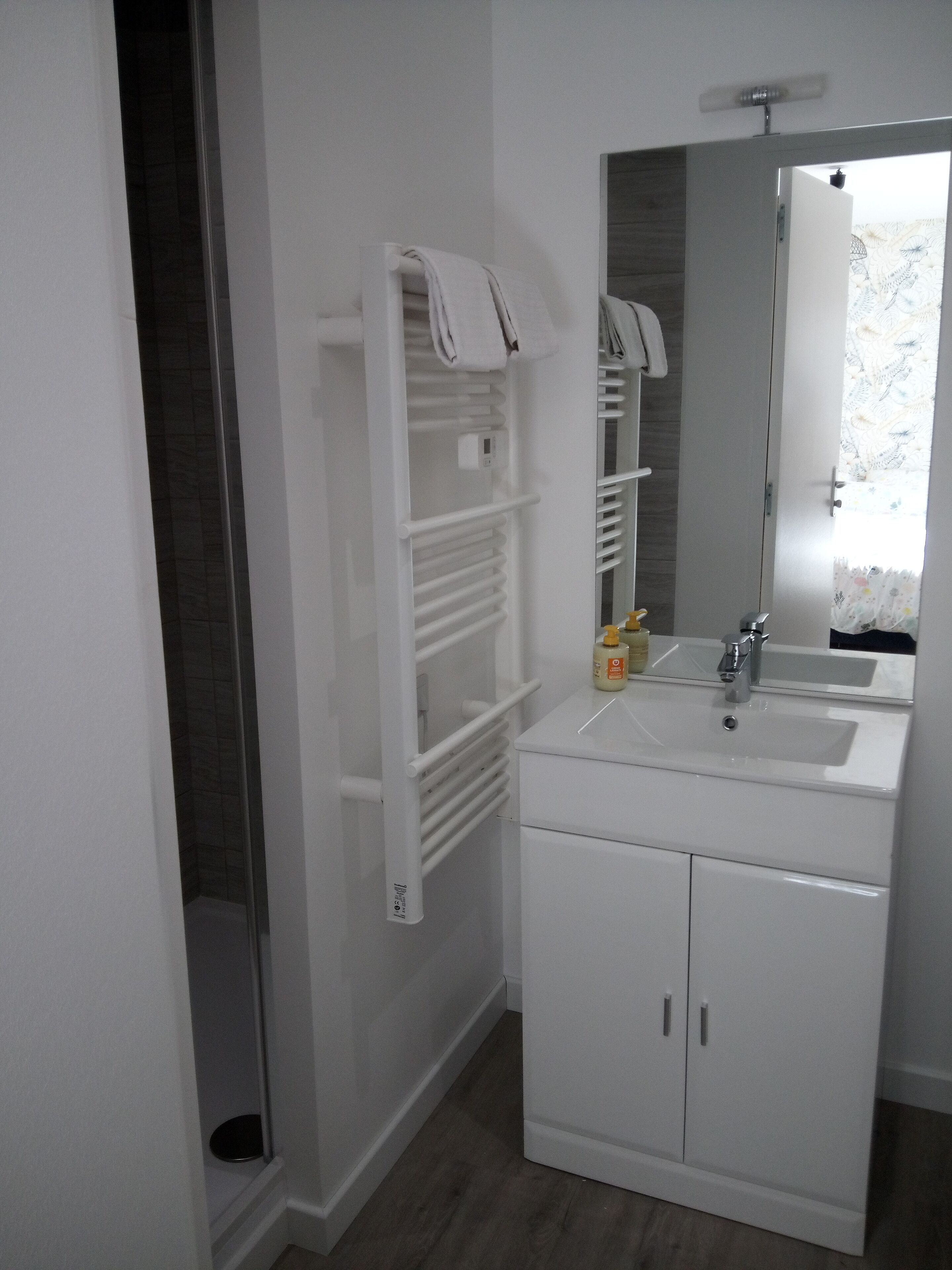 A bathroom with a white sink, mirror, and cabinet. There is a towel rack with towels and a bottle of hand soap on the sink.