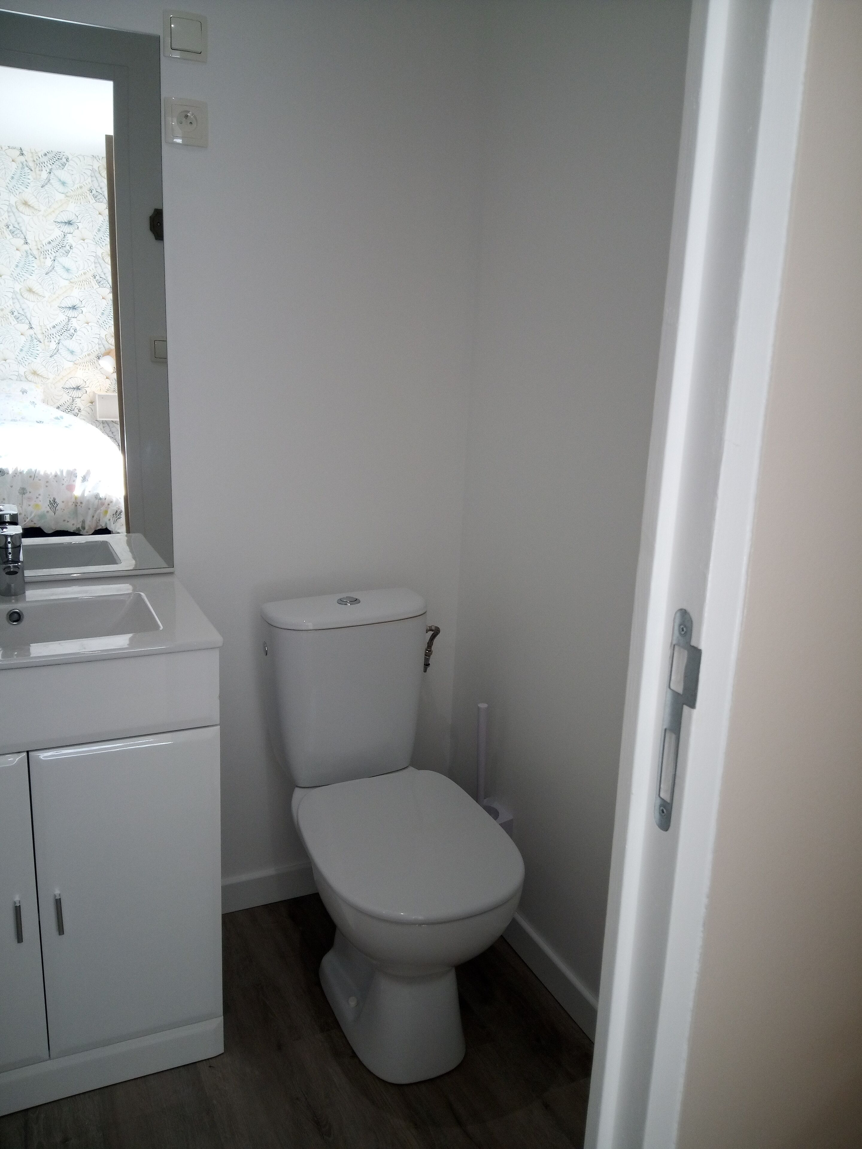 Ein kleines, sauberes Badezimmer mit Toilette, Waschbecken und Ablage.