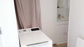A compact laundry area with a washing machine, a sink, and a mirror.
