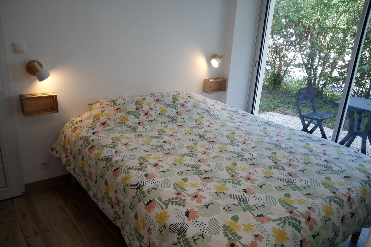 A bedroom with a floral bedspread, two wall-mounted lights, and a view of the outdoors through a large window.